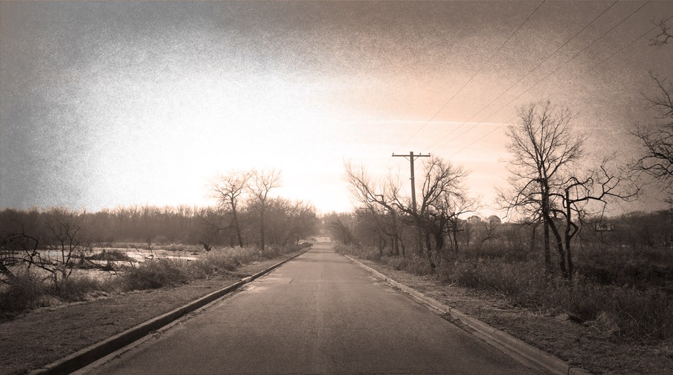 Archer Avenue, a haunted, paved road lined with bare trees, stretches into the horizon under a cloudy sky.