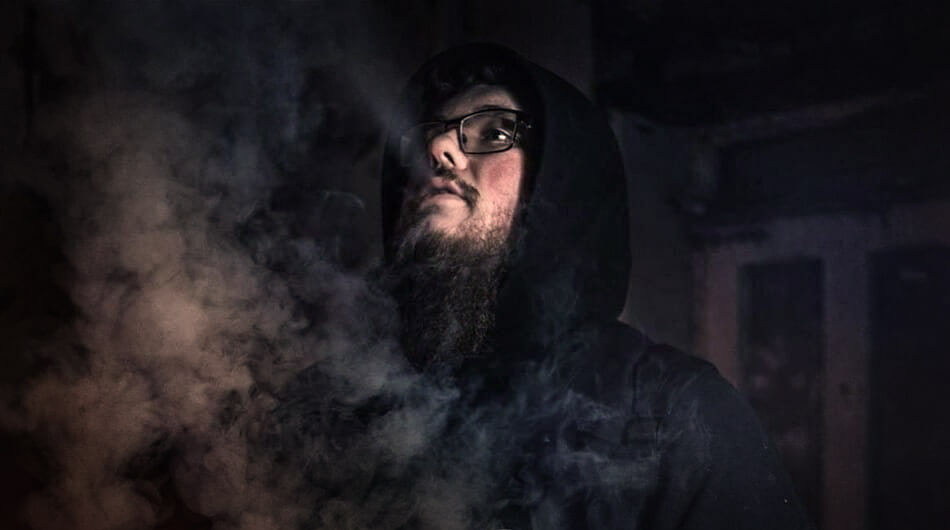 Matt with glasses and a dark hoodie looks upward, enveloped in swirling smoke, in a dimly lit environment—a scene straight out of a Dead City Paranormal episode. One of the popular youtube ghost hunters.