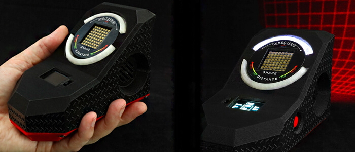 A hand holds a black GS2 Laser Grid System gadget which is a hexagonal-shaped electronic device used as a motion sensor when ghost hunting.