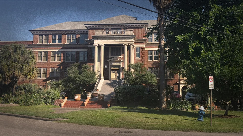 A three-story brick building called The Jefferson Davis Hospital. It's architecture features large columns and is surrounded by lush greenery and towering trees. From the nearby street, a stop sign sits. This building is one of the haunted places in Houston.