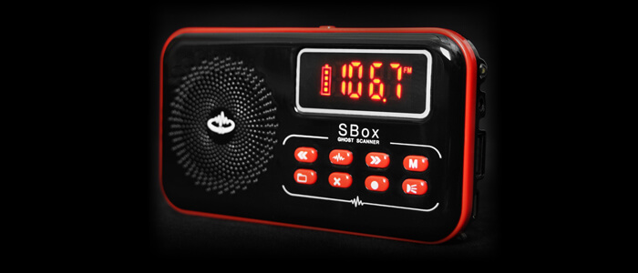 A black handheld ghost scanner with red accents displays the reading "106.7" on a digital screen. It features a circular speaker, control buttons, and the label "SBox Spirit Box," making it an essential addition to any Ghost Hunting Equipment List.