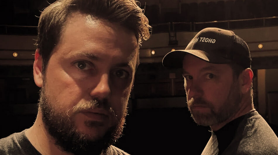Two youtube ghosthunters from The Haunted Side standing next to each other in an auditorium, recording a video for their YouTube channel.