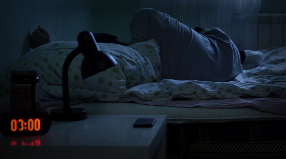 At 3:00 AM, a person lies in bed under a cozy blanket, the glow of a lamp casting soft shadows. The person asleep possibly having weird dreams which are more signs of a haunted house.